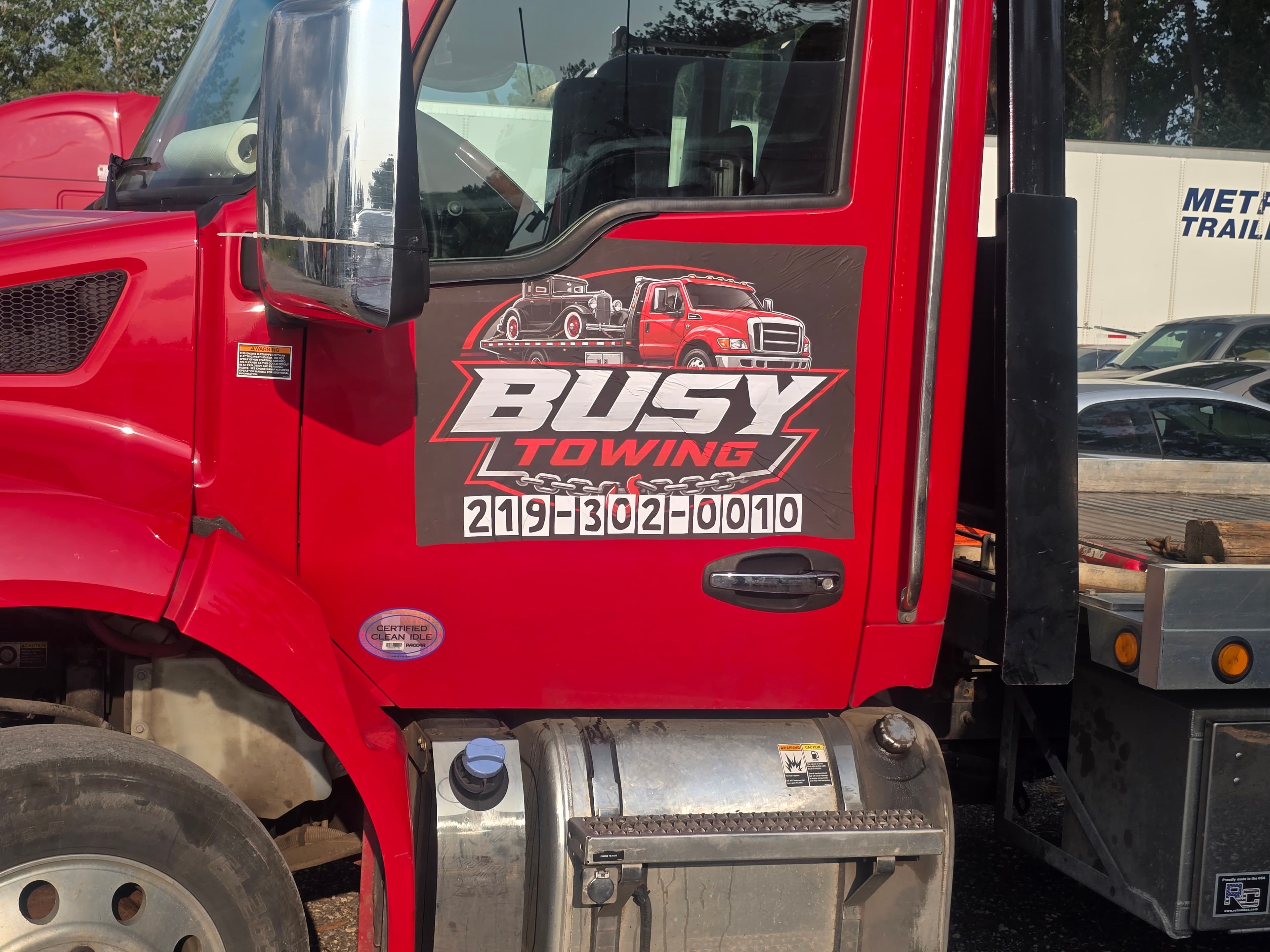 Red Busy Towing truck door with logo, phone number, and certified clean idle sticker.